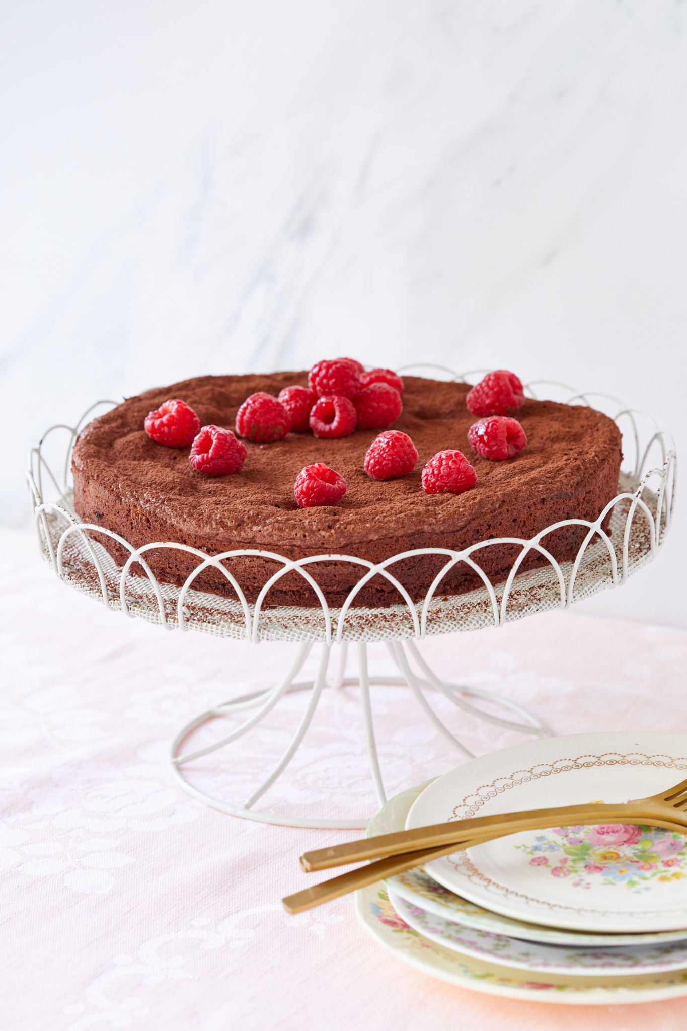 A Flourless Chocolate Almond Torte with raspberries, presented on a cake stand.