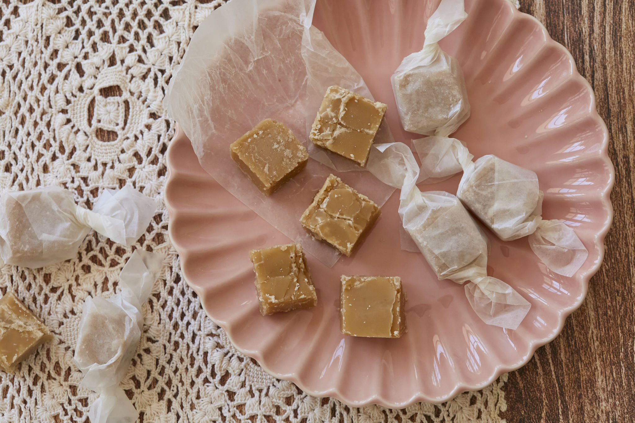 Homemade Maple Candy is served on a pink dish. A few pieces of the pure maple candies are wrapped in parchment paper.