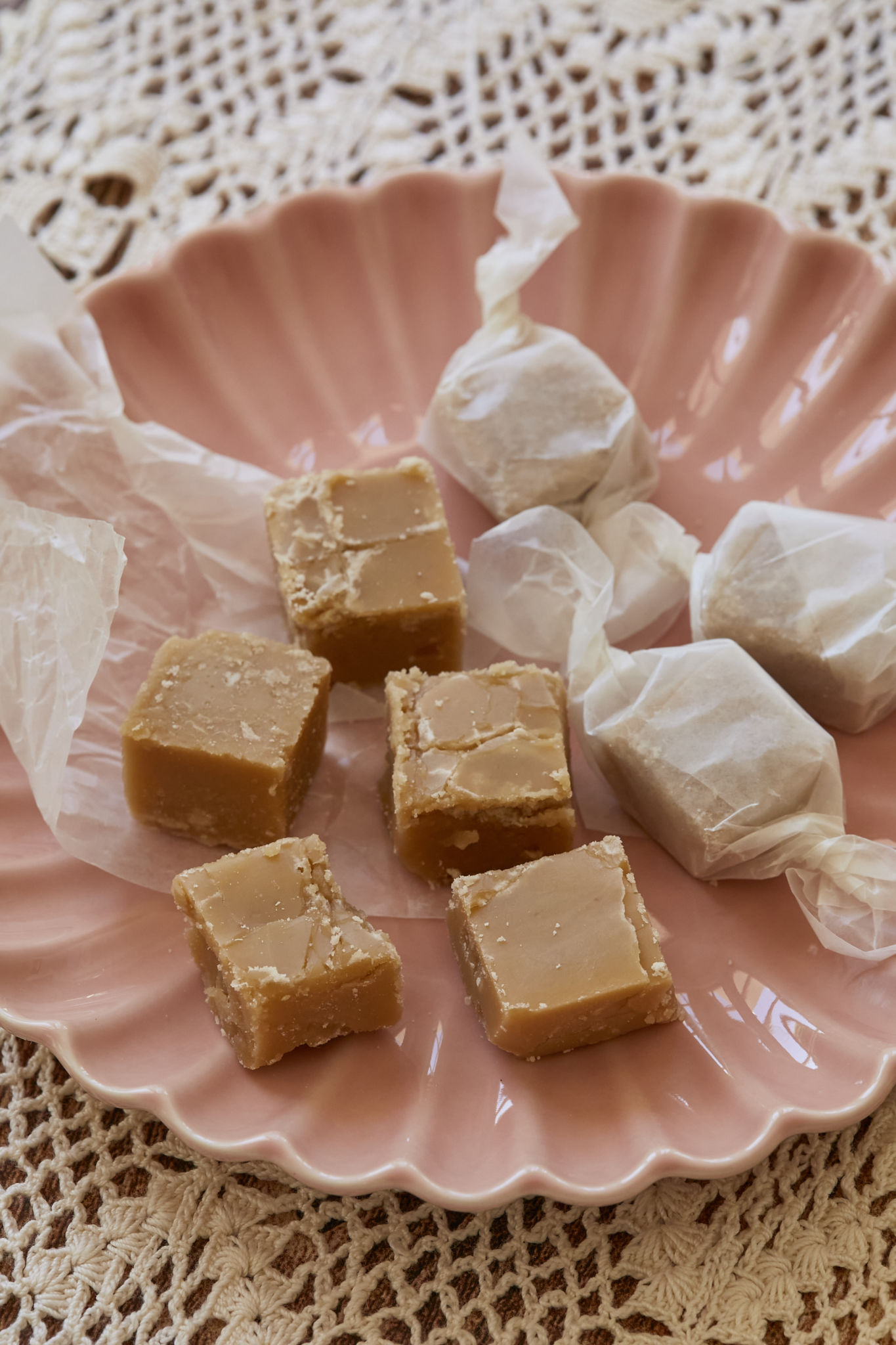 Square homemade candy made with maple syrup are served on a pink dish. The homemade candy is wrapped in wax paper