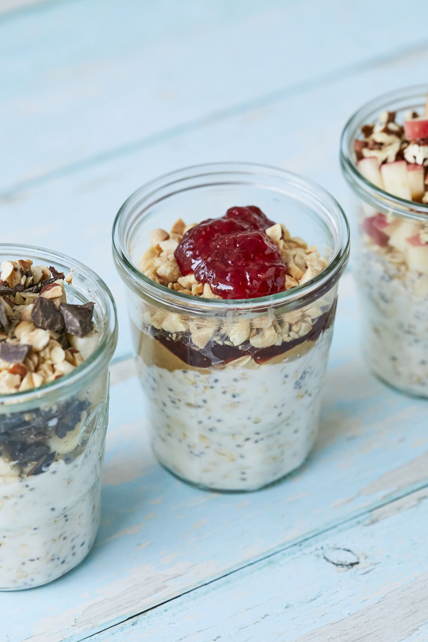 An additional sideview of the 3 jars of Overnight Oats so you can see the layers of ingredients in glass jars on a blue wooden table.
