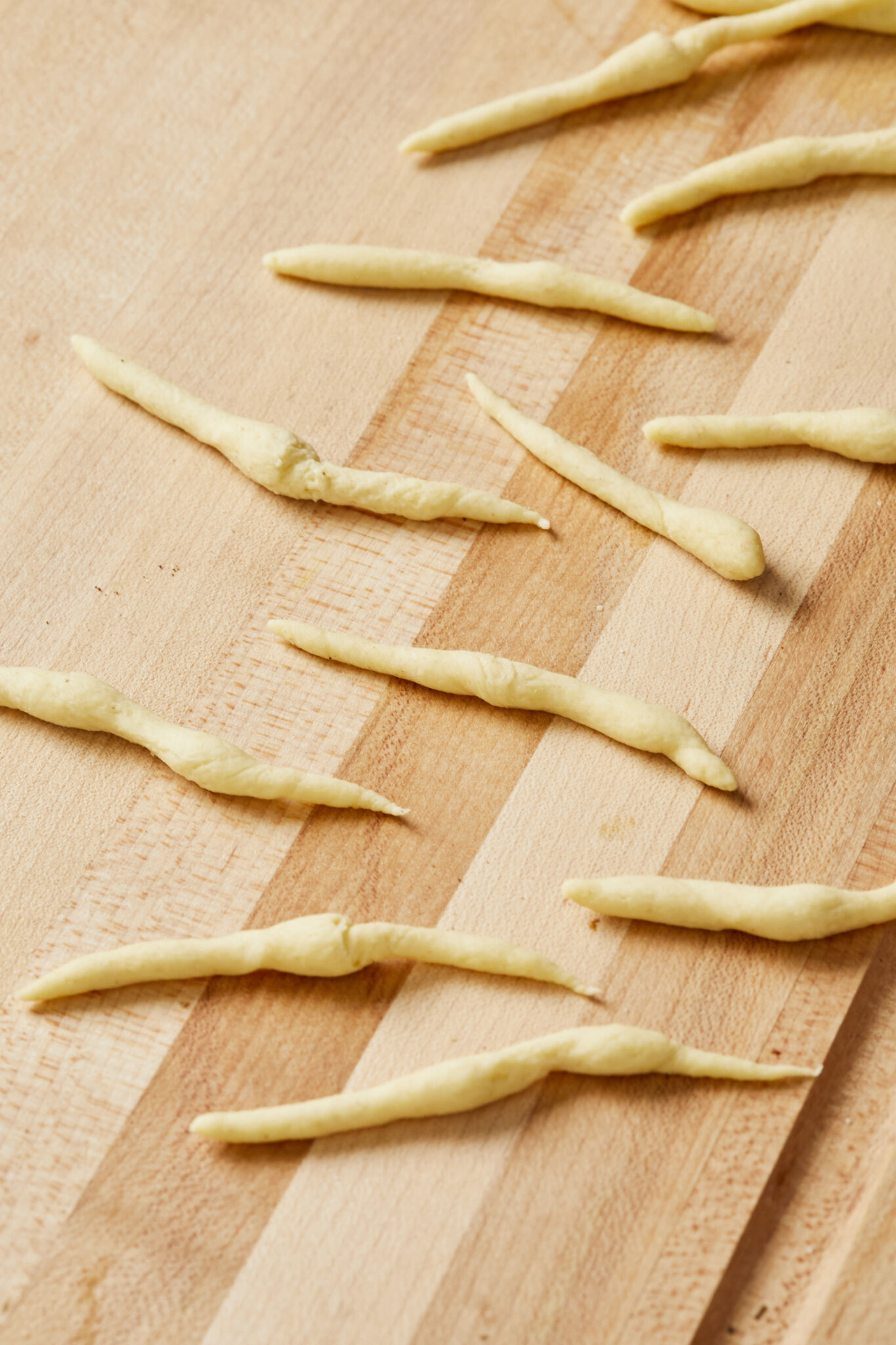 A close shot at Semolina Trofie pasta on a wooden board. They're in notable small, short, and irregular cylinder shape. 