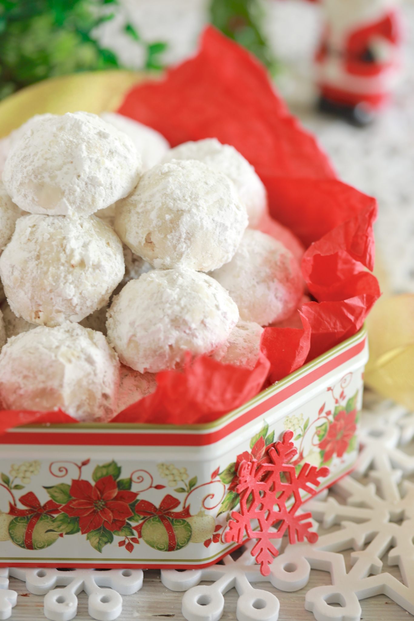 A batch of homemade Snowball Cookies are presented in a holiday tin with red tissue paper. 